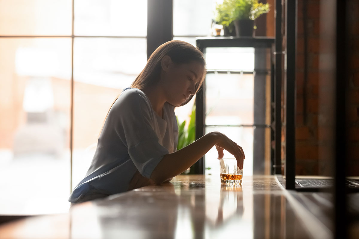 Women and Alcoholism Woman sitting at a bar thinking about her glass of alcohol