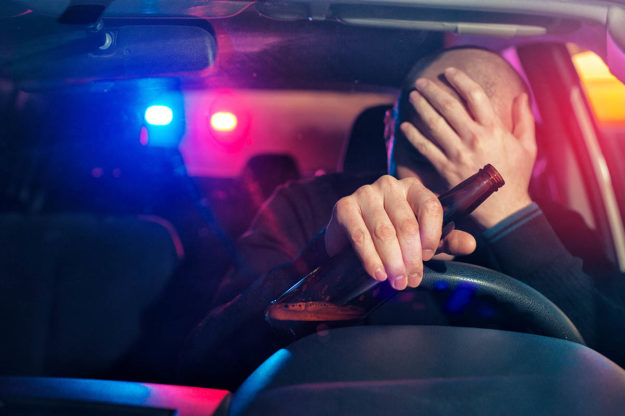 The Costs of Drunk Driving Man holding beer in hand pulled over for drunk driving